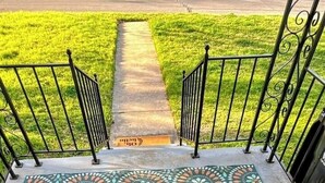 Un balcon doté d’un sol à motifs, de rampes en métal et offrant une vue sur une pelouse verdoyante et une route.