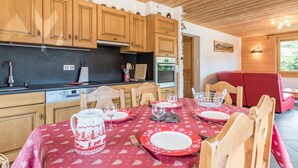 A cozy kitchen with wooden cabinets, a black countertop, and a dining area with a red tablecloth. - Cozy apartment in Les Gets with parking - sleeps 5 (Les Gets)