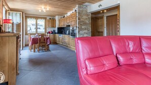 A cozy interior with a red leather sofa, wooden cabinets, a stone wall, and a dining area with a table and chairs. - Cozy apartment in Les Gets with parking - sleeps 5 (Les Gets)