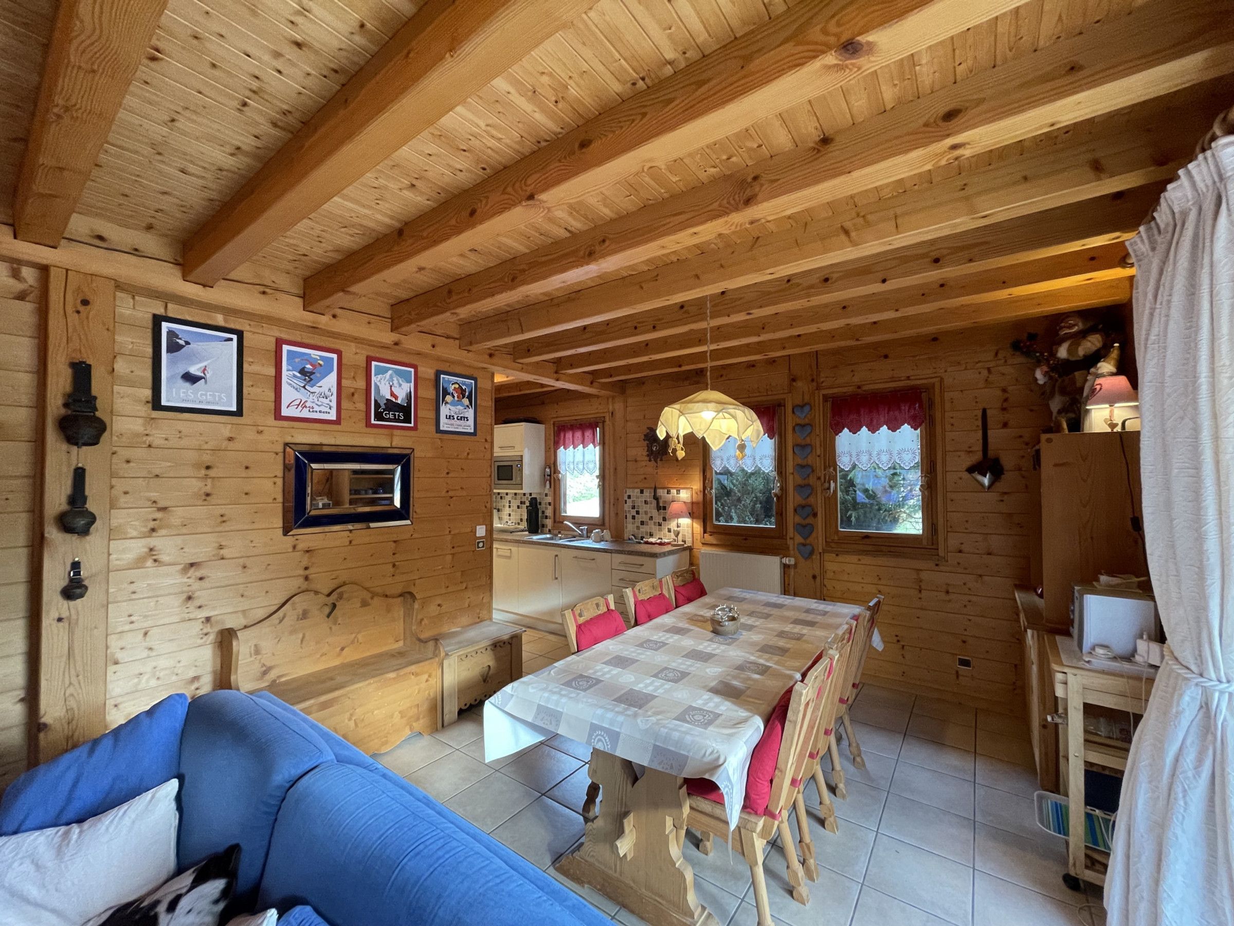 Interno di una baita in legno con tavolo da pranzo, sedie, divano, angolo cottura e quadri appesi alle pareti.
