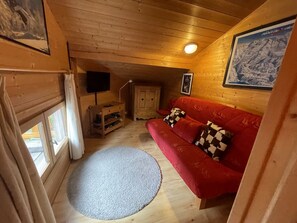 A cozy wooden cabin interior with a red sofa, a small wooden cabinet, a television, and a framed picture on the wall. - Family Chalet Les Gets with Wi-Fi and Parking (Les Gets)