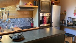 Een keuken met houten kastjes, een roestvrijstalen koelkast, een klok en een betegelde spatwand.