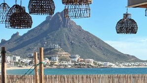 Een terras met tafels en stoelen met uitzicht op een strand en een berg.