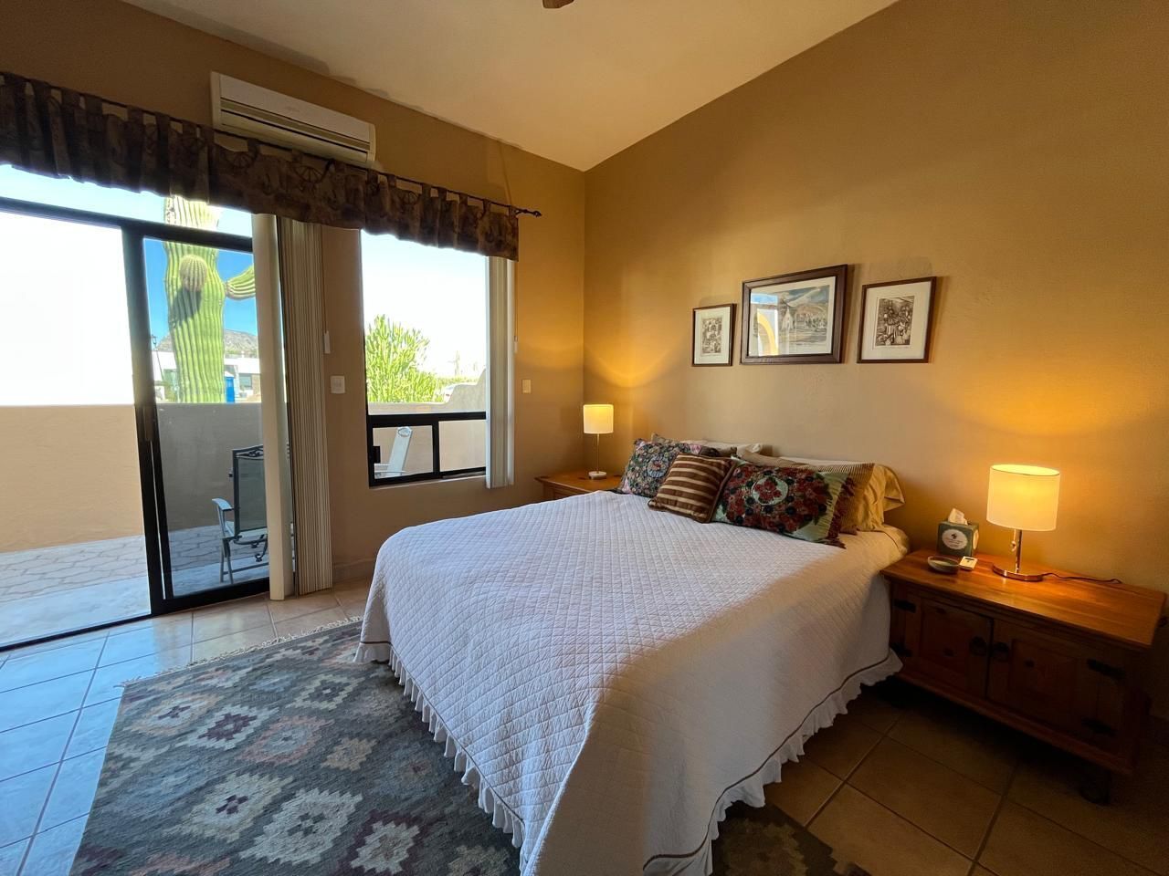 A bedroom with a large bed, a nightstand with a lamp, and a sliding glass door leading to a balcony.