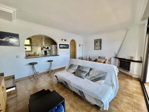 A living room with a sofa, a coffee table, a kitchen area with a counter and stools, and a fireplace. - Apartment in Roses with private parking, 2 bedrooms and large terrace (Roses)