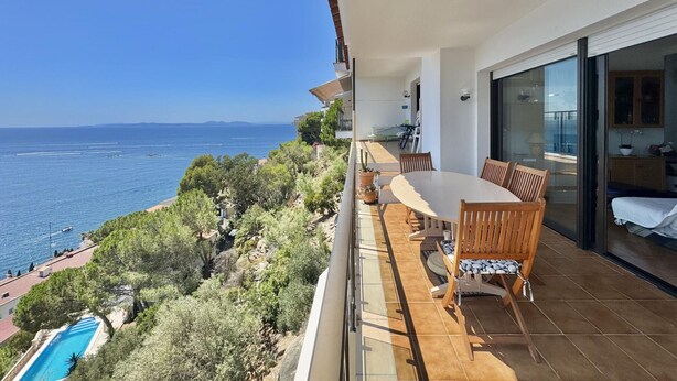 Ein Balkon mit Tisch und Stühlen mit Blick auf einen Pool und das Meer.