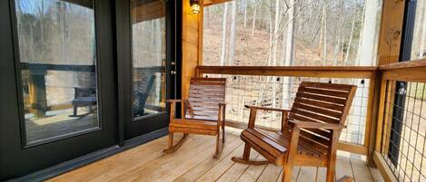 A wooden deck with two rocking chairs and a table, overlooking a forested area.