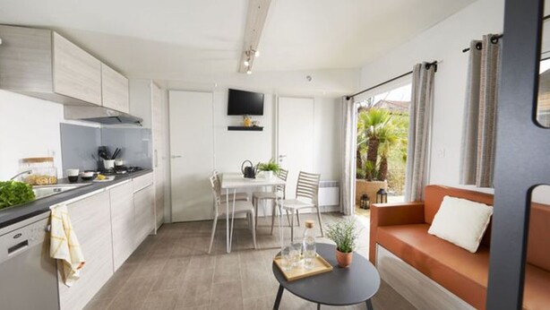 A modern kitchen with white cabinets, a dining area with a table and chairs, and a living area with a sofa and a coffee table.