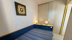 Quarto de hotel com uma cama, mesa de cabeceira com luminárias, uma obra de arte pendurada na parede e uma porta de madeira.