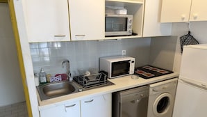 Uma cozinha compacta com armários brancos, uma lava-louças Bosch, micro-ondas e forno pequeno.