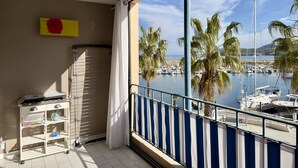 Uma varanda com vista para um porto, uma prateleira branca com objetos e um letreiro amarelo na parede.