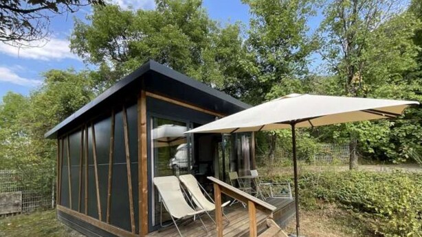 Eine kleine, moderne Hütte mit einer Holzterrasse und einem überdachten Sitzbereich im Freien.