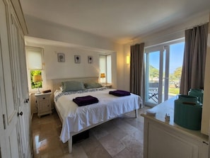 Ein Schlafzimmer mit Bett, Nachttischen, einem Schminktisch und einem Balkon mit Blick.