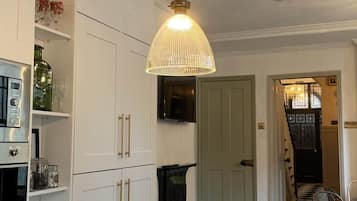 A kitchen with white cabinets, a white countertop, a hanging pendant light, and a view of a staircase leading to a dining area.