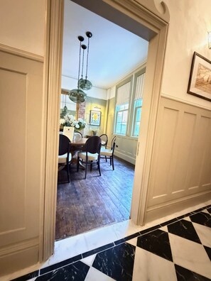 Un pasillo que conduce a un comedor con suelo de madera, una araña y un cuadro en la pared.