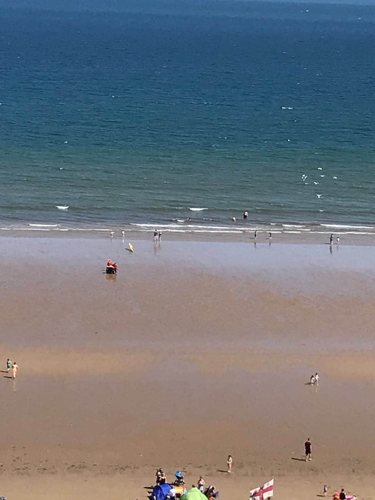 A beach with people walking and swimming, a flag, and a tent.