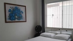 A bedroom with a bed, a fan, a window with curtains, and a painting on the wall. - casa/kitnet em São Jose na grande Florianópolis para ate 4 pessoas (São José)