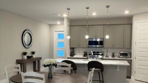 Una cocina moderna con una isla central, lámparas colgantes y un área de comedor con una mesa redonda y sillas.