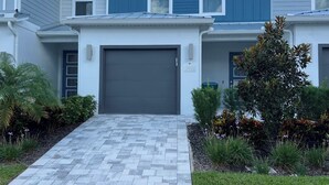 Una casa moderna de dos pisos con puerta de garaje gris, entrada pavimentada y jardines ajardinados.