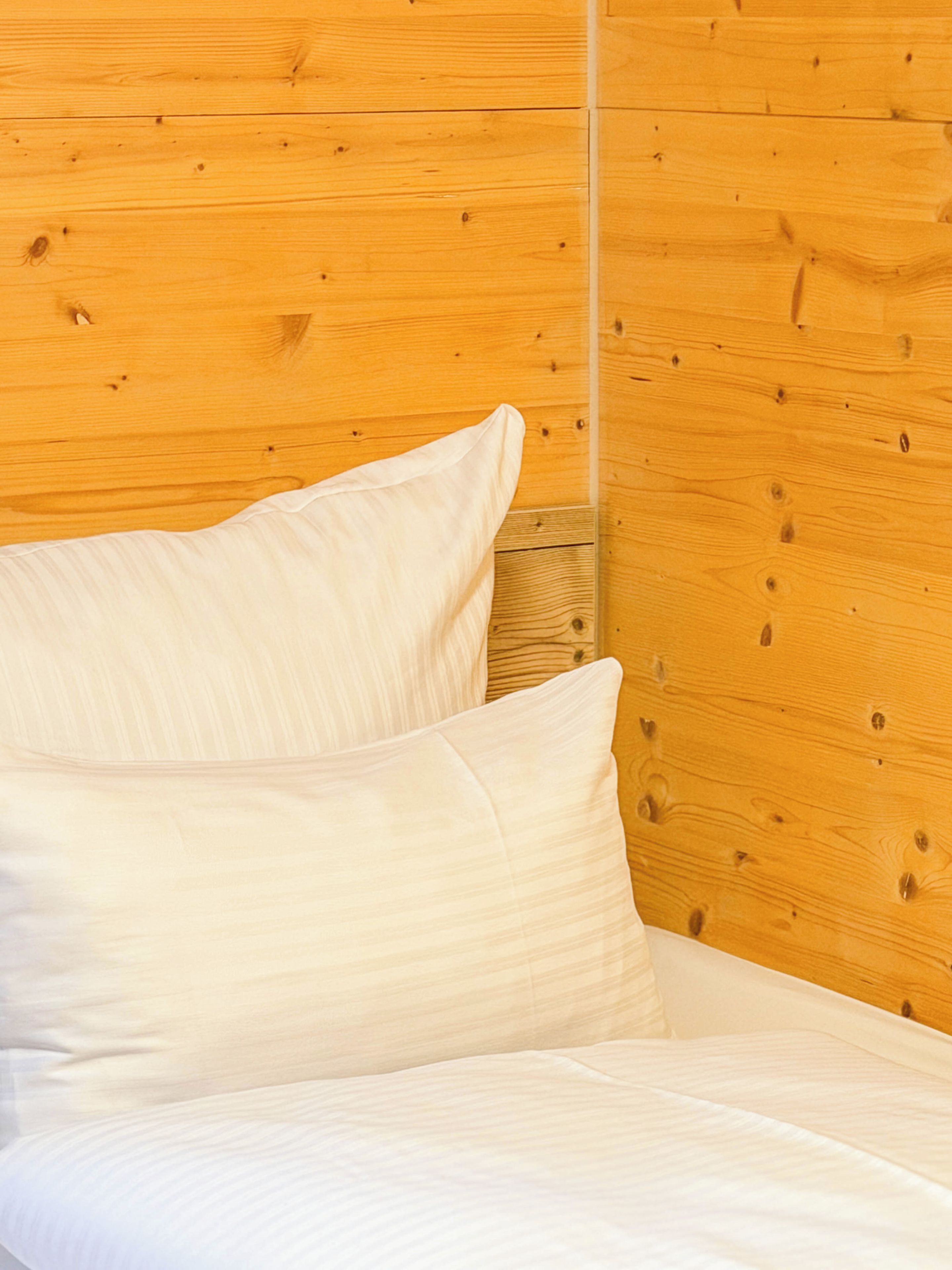 Una cama con ropa blanca frente a una pared de madera.
