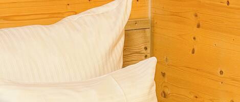 Una cama con ropa blanca frente a una pared de madera.