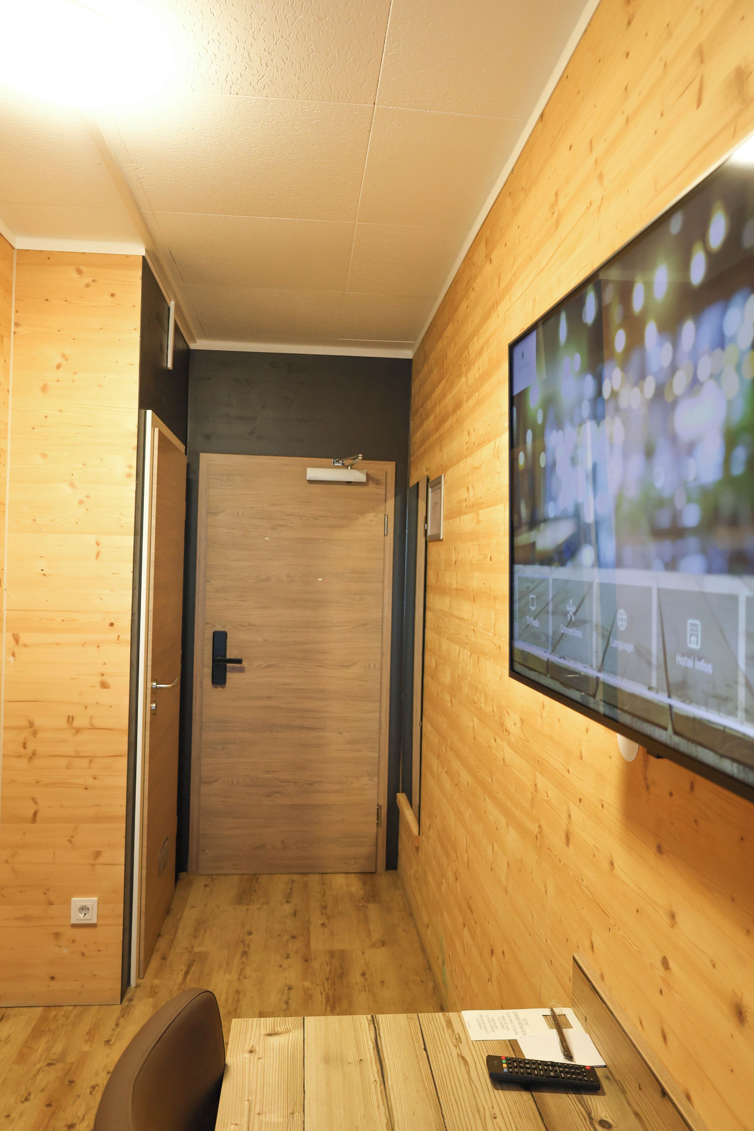 Ein Hotelzimmer mit Holzvertäfelung, einem an der Wand befestigten Fernseher und einem Schreibtisch mit Fernbedienung.