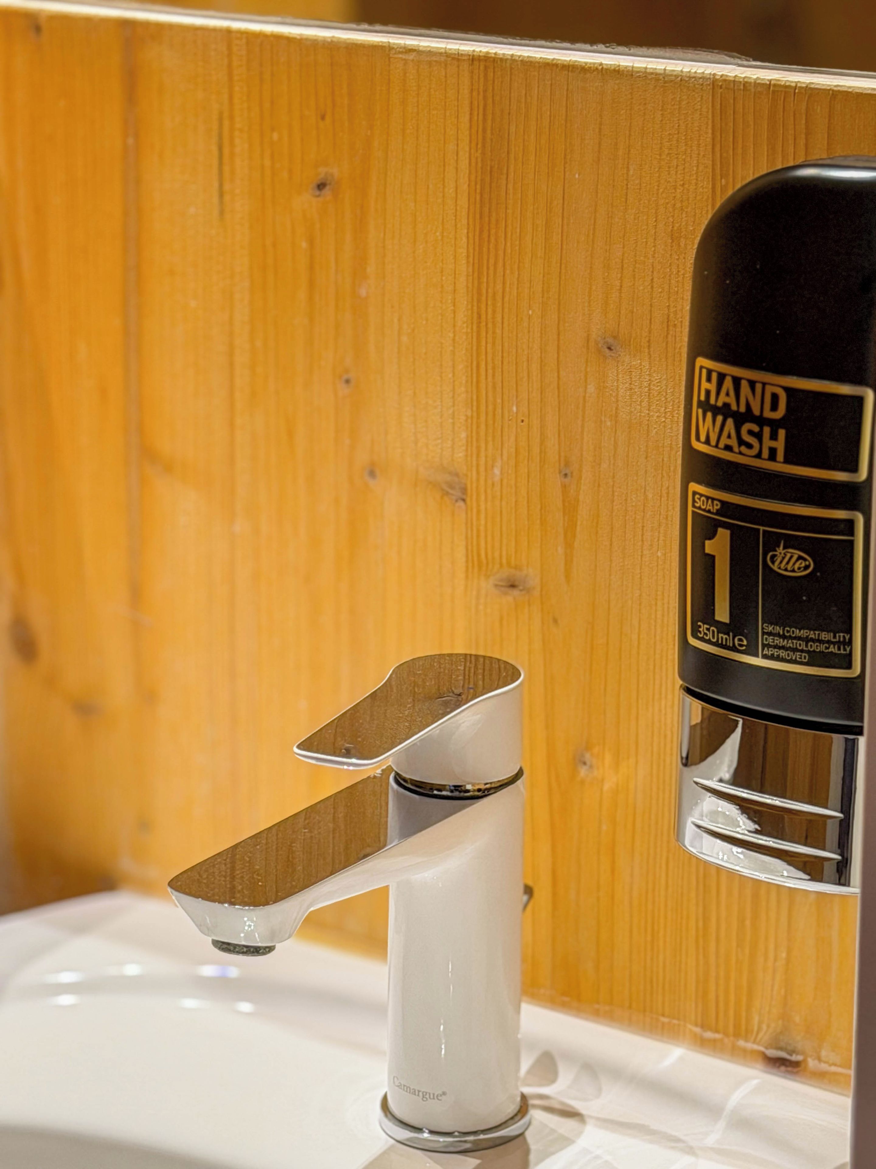 A hand wash dispenser with a soap dispenser attached to a chrome faucet.