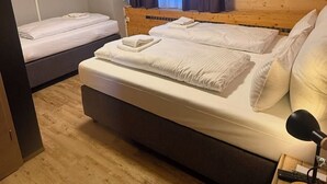 Ein Schlafzimmer mit einem großen Bett, einem kleineren Bett, einem an der Wand befestigten Fernseher und einem Fenster mit Vorhängen.
