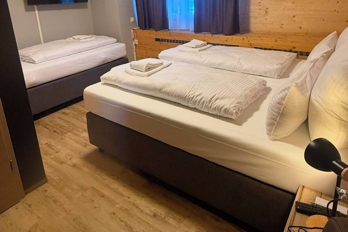 A bedroom with a large bed, a smaller bed, a TV mounted on the wall, and a window with curtains.
