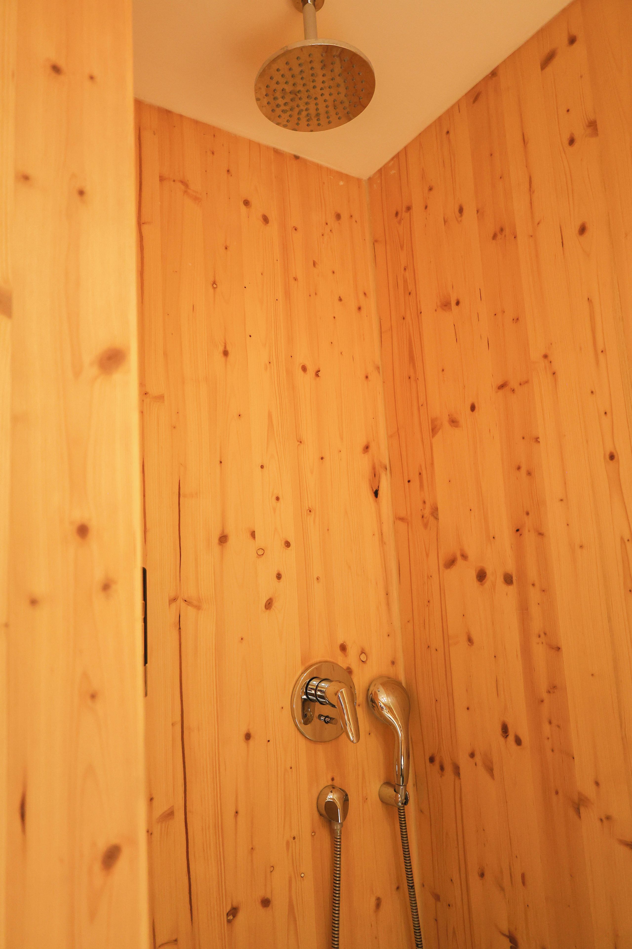 A wooden shower enclosure with a showerhead and hose.