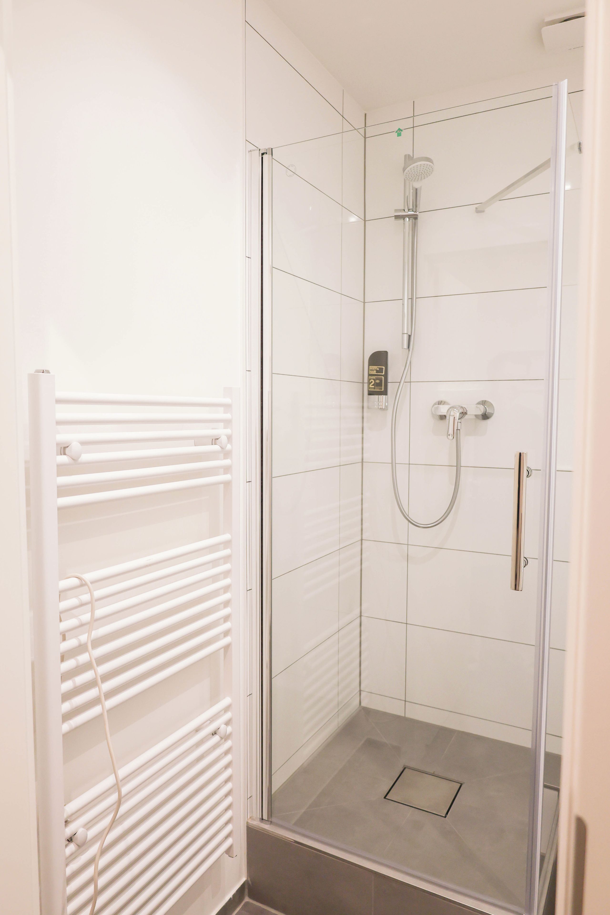 A glass-enclosed shower with a handheld showerhead, a control panel, and a white radiator.