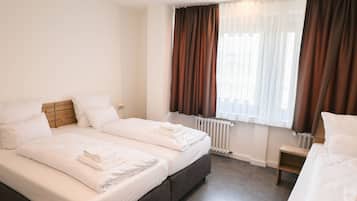 A hotel room with two beds, a radiator, and a window with curtains.