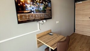 Ein modernes Zimmer mit einem an der Wand befestigten Flachbildfernseher, einem Holztisch, einem braunen Stuhl und Holzboden.