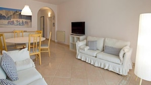 Un salón con un sofá blanco, una mesa de comedor con sillas, un televisor y un cuadro en la pared.