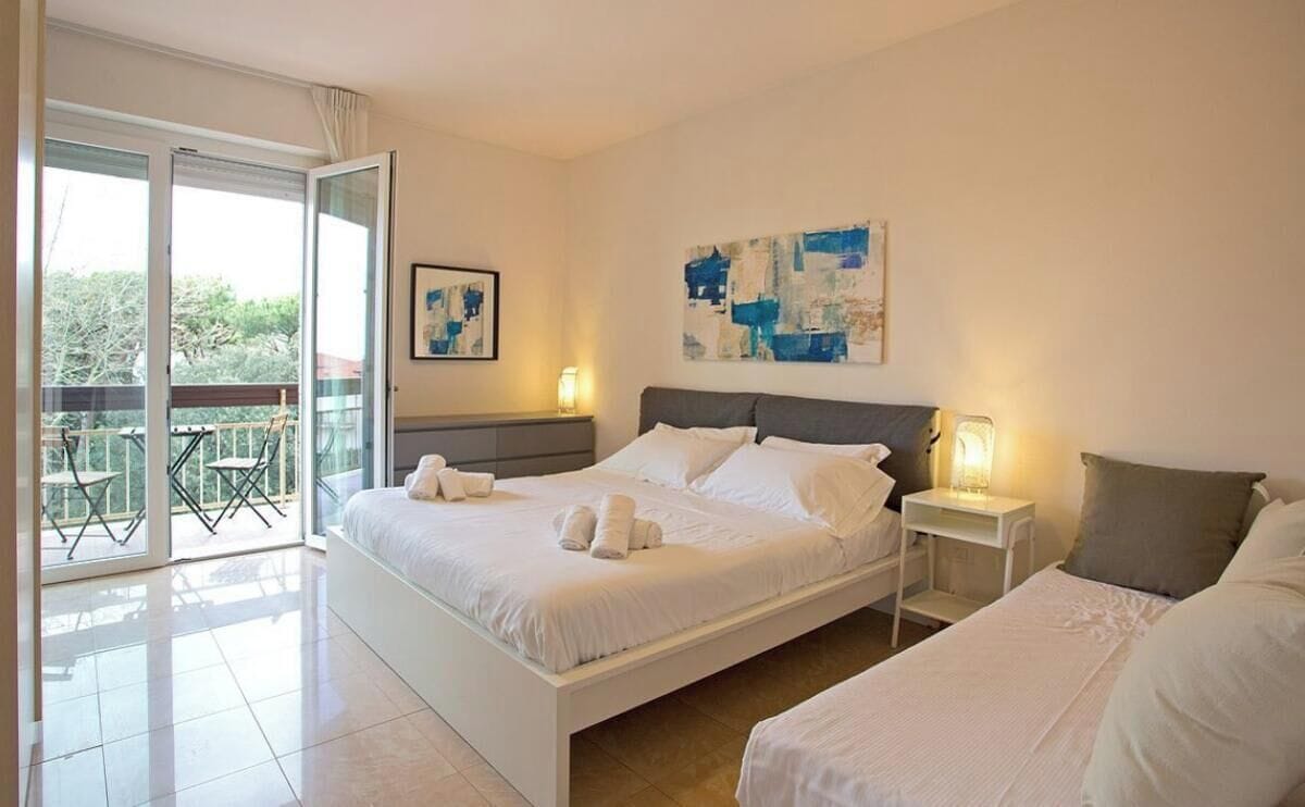 Ein Schlafzimmer mit einem großen Bett, einem kleineren Bett, einem Nachttisch mit Lampe und einem Balkon mit Sitzgelegenheiten.