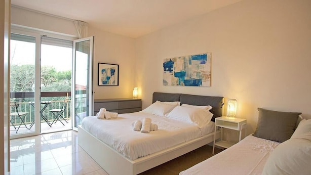 Un dormitorio con una cama grande, una cama más pequeña, una mesita de noche con lámpara y un balcón con sillas.