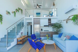 A modern living room with a staircase, a dining area, a kitchen, and a balcony with plants.