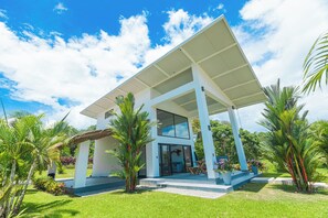 A modern house with a covered patio, large windows, and lush greenery.