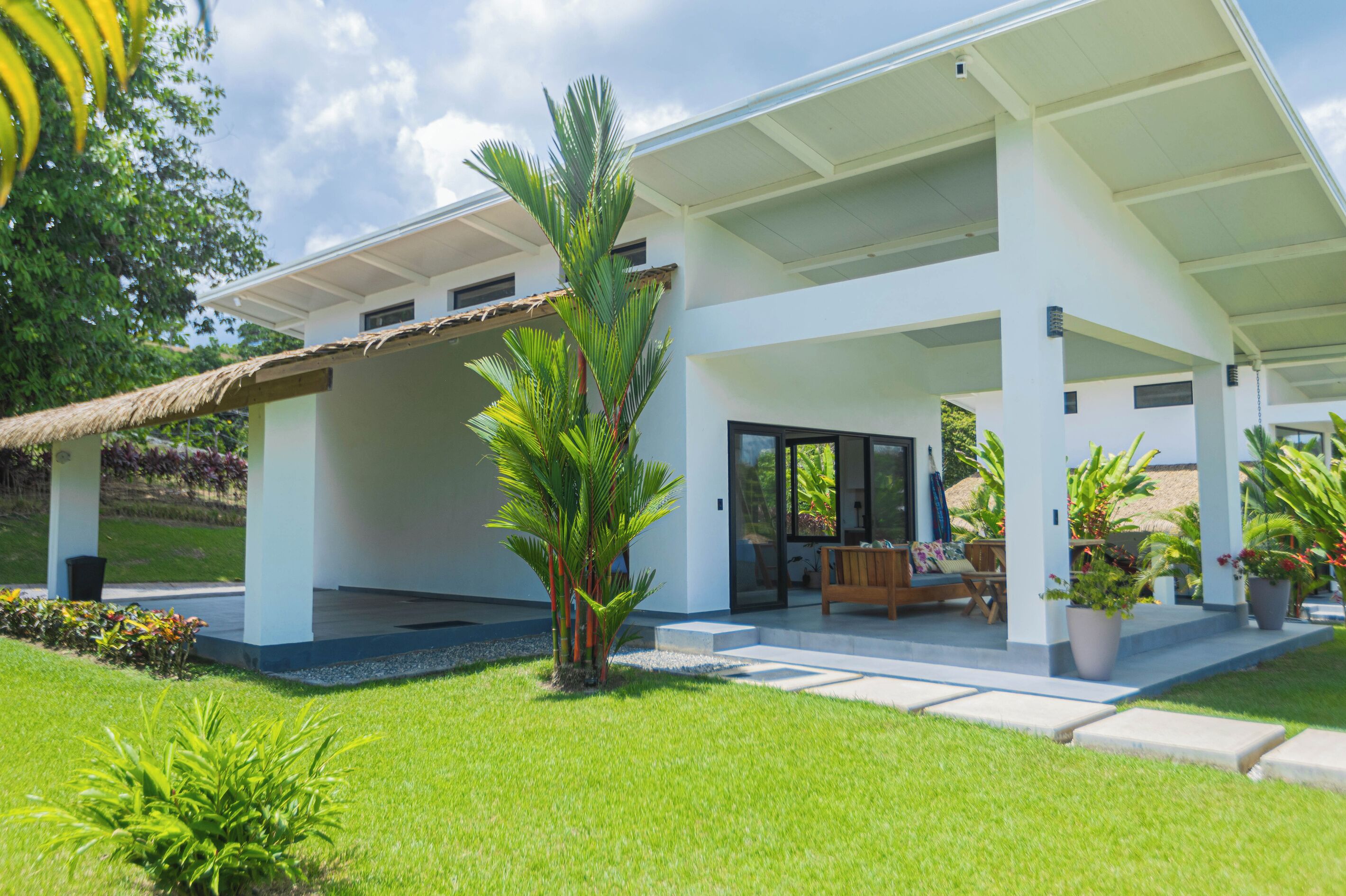 A modern house with a covered patio, a lawn, and a palm tree.