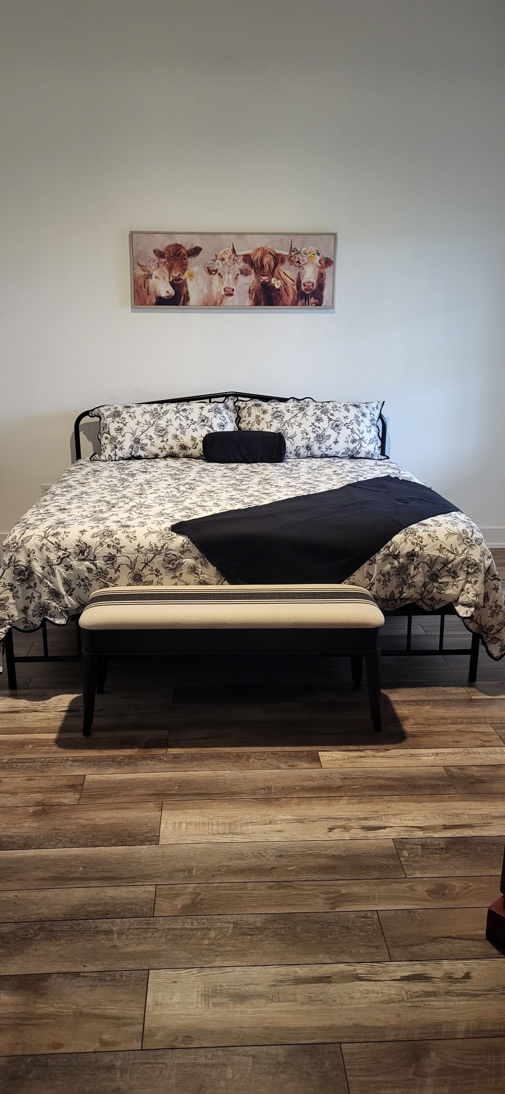 A bed with floral bedding, a black throw, and a bench.