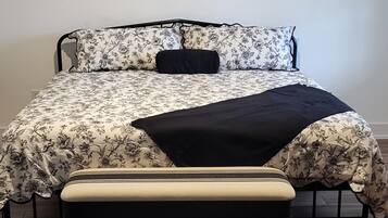 A bed with floral bedding, a black throw, and a bench.