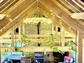 An attic room with wooden beams, a stone wall, and a hanging light fixture. - Exclusive Vineyard Estate for 18 Guests (Carmarthenshire)