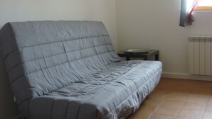 Una habitación con sofá gris, un radiador, una mesita y una ventana con cortinas.