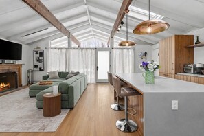 Una sala de estar moderna con un sofá seccional verde, una chimenea y una zona de cocina con armarios de madera y un taburete de bar.