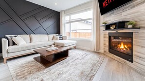 Ein modernes Wohnzimmer mit einem Ecksofa, einem Couchtisch, einem Kamin und einem großen Fernseher, der das Netflix-Logo zeigt.