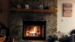 Een stenen open haard met een brandend vuur, een welkomstbord erboven, en een muur met een bord waarop deugden staan.
