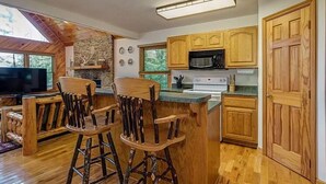 A kitchen with wooden cabinets, a microwave, a stove, and a bar area with stools. - Quiet Cabin in Murphy, NC 20 min drive to Blue Ridge, GA & Copperhill, TN (Murphy)