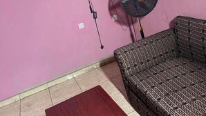 Una habitación con pared rosa, un sofá estampado, una mesa de madera, un televisor montado en la pared y un ventilador de pie.