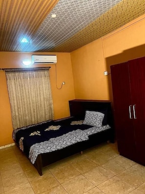 Une chambre à coucher comprenant un lit, un appareil de climatisation, une armoire et un plafond décoré de motifs.