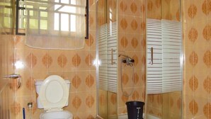 Un baño con inodoro, cabina de ducha y un balde.
